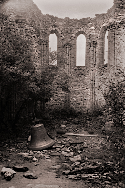 Chapelle en ruine à contrejour, avec une cloche sur le sol